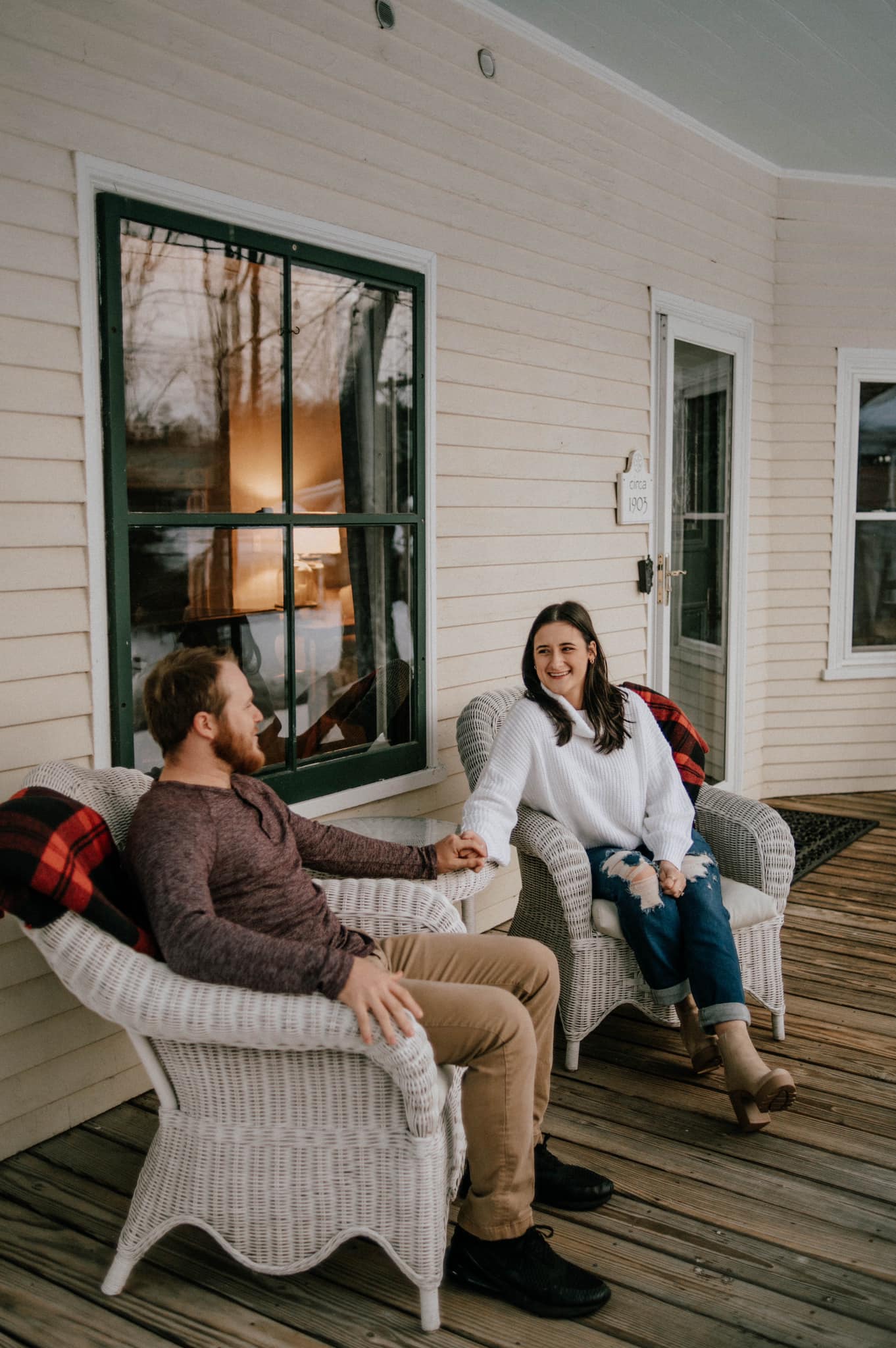 couple holding hands sitting in wicker chairs on front porch